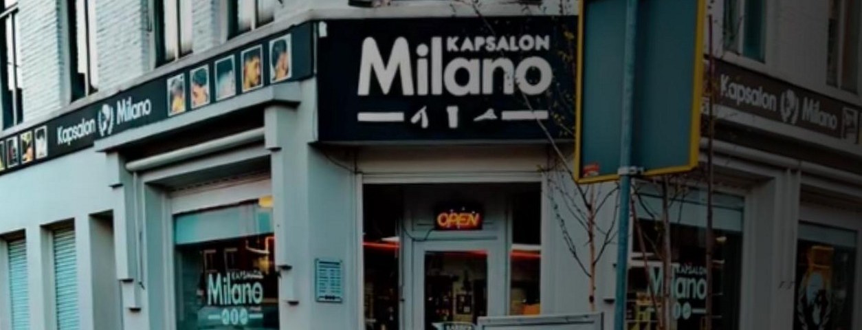 De gevel van Kapsalon Milano op de Markt in Oudenbosch, met het zwarte bord met Milano erop en een verlicht OPEN-bord in de deur