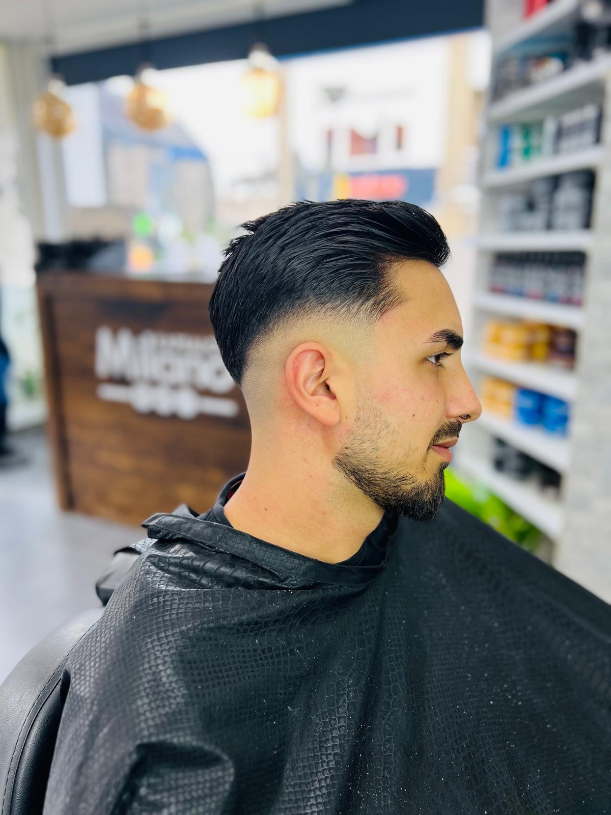Een klant met een korte fade en een lange, achterover gekamde bovenkant, van opzij, met de balie van Milano op de achtergrond