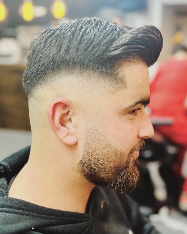 Een klant met een fade, een volle bovenkant en een bijgewerkte baard, van opzij